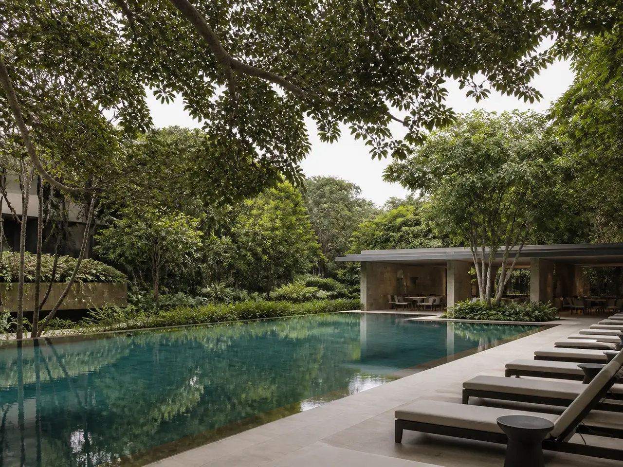 Quiet outdoor pool surrounded by dense planting and a contemporary pavilion